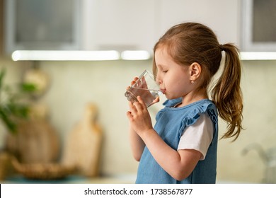 Cute Little Girl Drinking Water In Kitchen At Home. Child Hold Glass Clean Filtered Drinking Water In His Hands And Drinks It With Pleasure To Quench His Thirst. Water Balance. Prevention Constipation