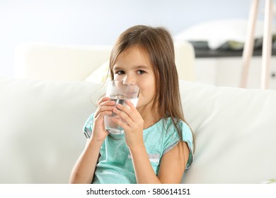 Cute Little Girl Drinking Water On Sofa At Home