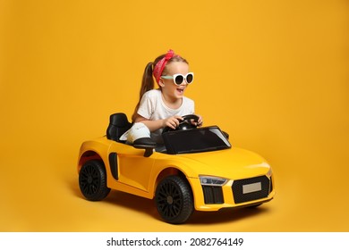 Niña pequeña linda conduciendo el auto de juguete eléctrico de los niños sobre fondo amarillo