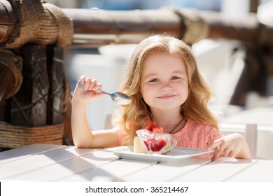 cute little girl eating cake. pretty little girl with cake and strawberries. child eating dessert. girl eating with spoon by the table