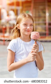 Cute Little Girl Eating Candy Apple At Fair In Amusement Park.