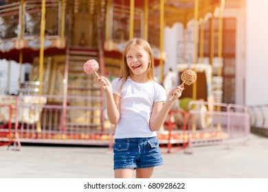 Cute Little Girl Eating Candy Apple And Posing At Fair In Amusement Park.