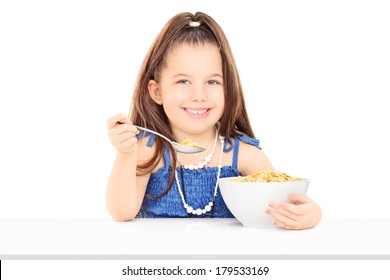 Cute little girl eating cereal from a bowl isolated on white background