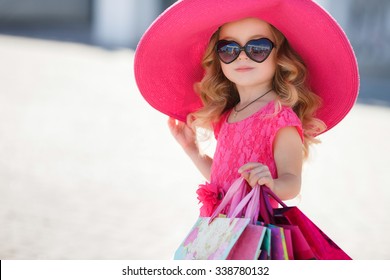 cute little girl in fashionable hat on shopping. portrait of a kid with shopping bags. child in dress, sunglasses and shoes near shopping mall having fun. shopping. girl. fashion