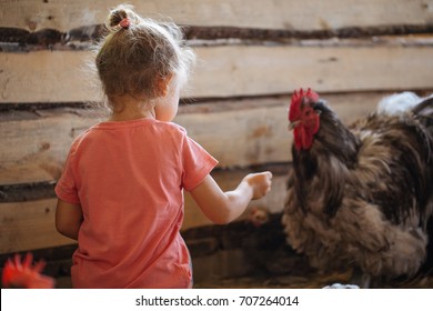 Cute little girl feeding chickens at hen house in countryside, rear view