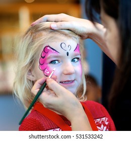 Cute Little Girl Getting Her Face Painted Like A Butterfly By Face Painting Artist. Kids Animation At The Party.