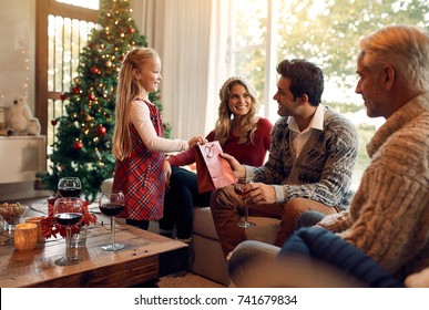 Cute Little Girl Giving Christmas Gift To Her Father. Happy Family Sitting Together In Living Room Exchanging Presents.