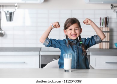 Cute little girl with glass of milk at table in kitchen