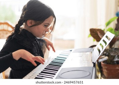 A cute little girl with glasses and a braid is learning to play the piano in a black dress. - Powered by Shutterstock