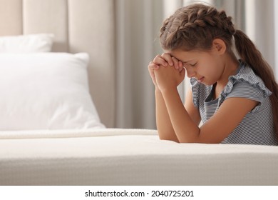 Cute little girl with hands clasped together saying bedtime prayer at home. Space for text