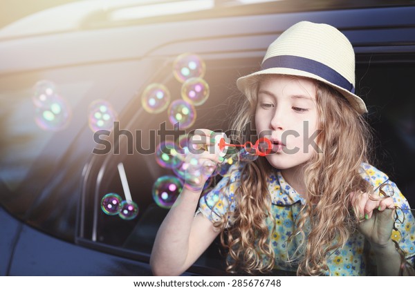 Cute\
little girl in a hat lets soap bubbles in car\
window