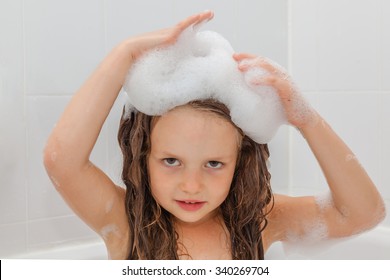 Cute Little Girl Having A Bath In Foam Water. Child Washing Her Long Hair.  Close Up. Selective Focus On Kids Face.