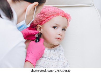 Cute Little Girl Having Ear Piercing Process With Special Piercing Gun In Beauty Center By Medical Worker