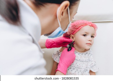 Cute Little Girl Having Ear Piercing Process With Special Piercing Gun In Beauty Center By Medical Worker