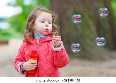 Cute little girl having fun with soap bubbles in summer park