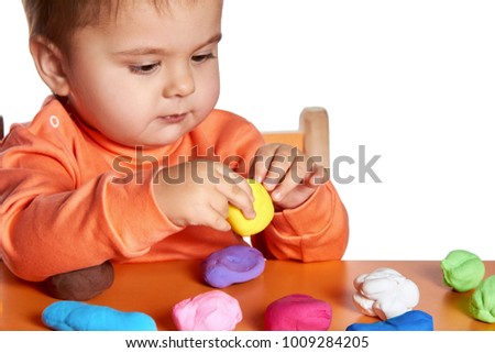 Cute little girl having fun with colorful modeling clay isolated on white background. Creative kid molding at the table. Child play with plasticine or dough.