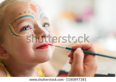 Cute little girl having her face painted for Halloween party. Halloween or carnival family lifestyle background. Face painting, headshot close up.