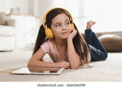 Cute Little Girl With Headphones And Tablet Listening To Audiobook At Home