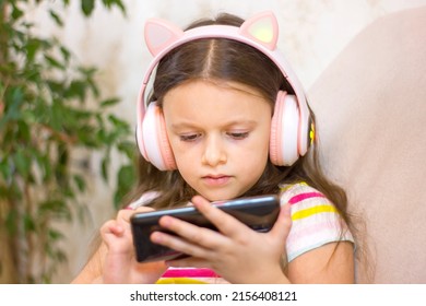 Cute Little Girl In Headphones Is Using A Smartphone. Selective Focus. Closeup Portrait. Kid Using Technology.