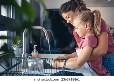 A cute little girl helps her mother washing dishes. Child doing house chores. Mother teaches a child to wash dishes. - Powered by Shutterstock