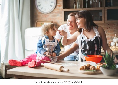Cute little girl and her beautiful parents are smiling while cooking in kitchen at home - Shutterstock ID 1120755581