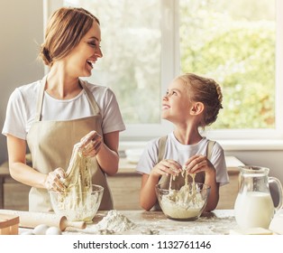 Cute Little Girl and Her Beautiful Mom in Aprons Looking at Each Other. Family Smiling While Kneading Dough in Modern Kitchen at Sweet Home. Happy Smiling Family Cooking Tasty Biscuit. - Powered by Shutterstock