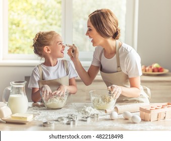 Cute little girl and her beautiful mom in aprons are playing and laughing while kneading the dough in the kitchen - Powered by Shutterstock