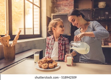 Cô bé dễ thương và mẹ xinh đẹp của cô đang mỉm cười trong khi uống sữa và ăn bánh nướng xốp trong nhà bếp. Mẹ đang rót sữa