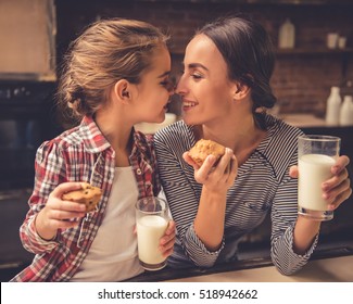 Cute little girl and her beautiful mother are touching noses and smiling while drinking milk and eating muffins