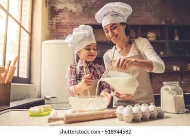 Cute little girl and her beautiful mother in chef hats are mixing muffin batter in the bowl and smiling while preparing it for baking. Mother pouring milk - Powered by Shutterstock