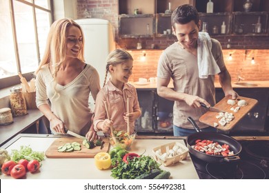 Cute kleine Mädchen und ihre wunderschönen Eltern lächeln, während sie zu Hause in der Küche kochen