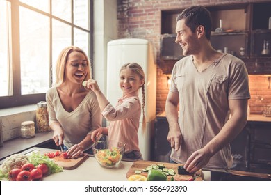 Cute little girl and her beautiful parents are cutting vegetables and smiling while cooking in kitchen at home - Shutterstock ID 556492390