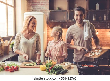 Cute little girl and her beautiful parents are  smiling while cooking in kitchen at home - Shutterstock ID 556492762