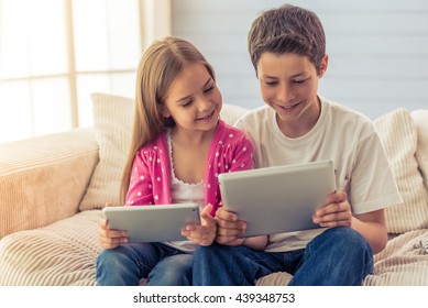 Cute little girl and her brother are using tablets and smiling, sitting on sofa at home - Powered by Shutterstock