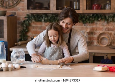 Cute little girl and her father in aprons rolling out the dough together on kitchen table, making cookies, free space - Powered by Shutterstock