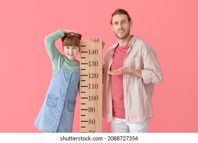 Cute little girl and her father measuring height on color background