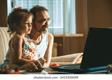 A cute little girl and her grandfather using a laptop, demonstrating a modern-day moment of connection and digital interaction. Two generations learning how to use technologies. - Powered by Shutterstock