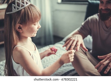 Cute Little Girl And Her Handsome Bearded Dad Are Playing In Her Room. Girl Is Painting Her Dad Nails