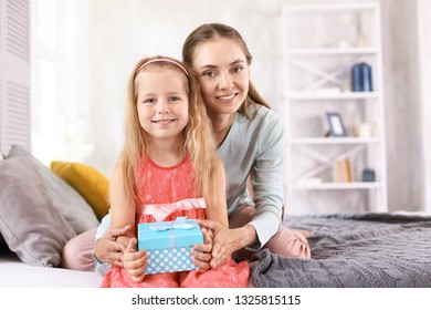 Cute little girl with her mom and gift box sitting on bed at home