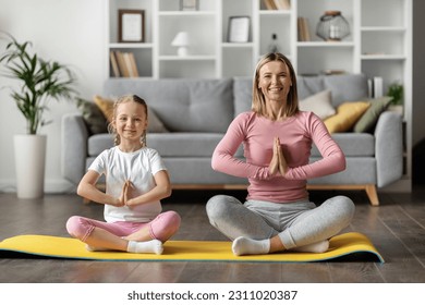 Cute Little Girl And Her Mom Practicing Yoga At Home, Happy Family Mother And Female Child Meditating Together In Living Room Interior, Sitting In Lotus Position And Smiling At Camera - Shutterstock ID 2311020387