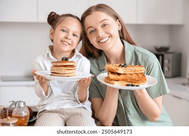 Cute little girl and her mother holding tasty pancakes with waffles in kitchen - Powered by Shutterstock