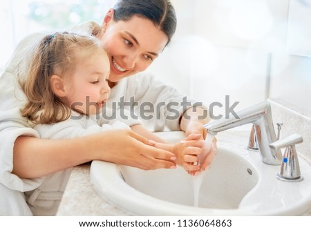 Cute little girl and her mother are washing hands under running water.