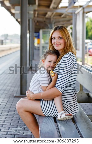 Cute little girl and her mother on a railway station. Kid and woman waiting for train and happy about a journey. People, travel, family, lifestyle concept
