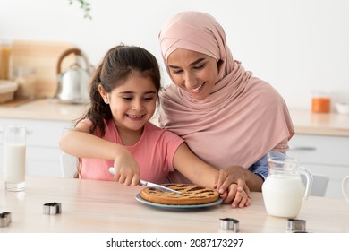 Cute Little Girl And Her Muslim Mother In Hijab Cutting Homemade Pie In Kitchen, Religious Arab Woman And Happy Female Child Ready To Taste Sweet Pastry, Enjoying Baking Together At Home, Closeup