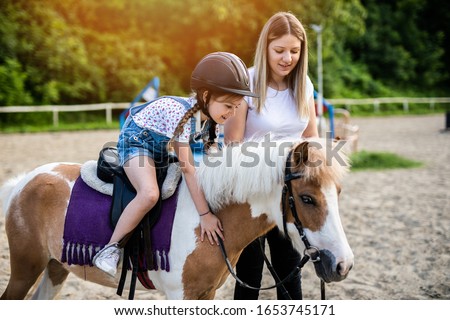 Cute little girl and her older sister enjoying with pony horse outdoors at ranch.
