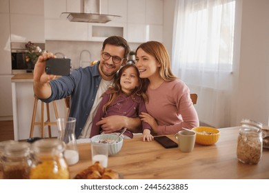 Cute little girl and her parents taking selfie using a smart phone in kitchen at home - Powered by Shutterstock