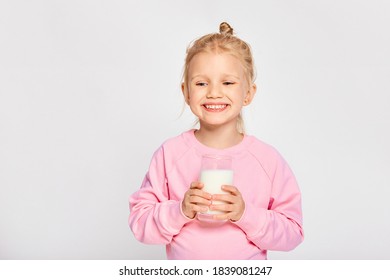 Cute Little Girl Holding A Large Glass Of Milk. Kid 4-5 Year Old Posing In Studio On Gray Background