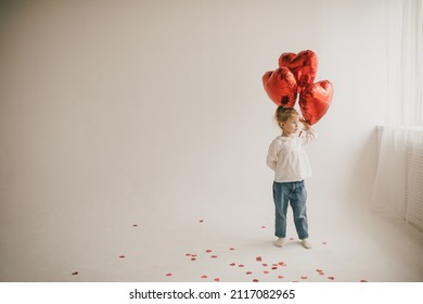 Cute little girl holding red heart shaped balloons on white background. Saint Valentine's Day celebration.