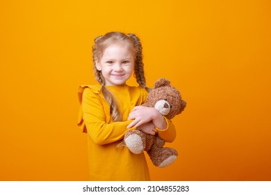 cute little girl holding a teddy bear on a yellow background, hugging - Powered by Shutterstock