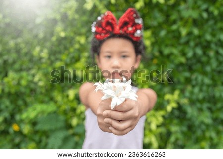 Cute little girl holding white tree jasmine flower against green nature background. Daughter give her mother flowers.